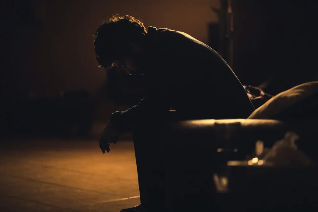 Person sitting alone in a dimly lit room, appearing emotionally distressed and withdrawn
