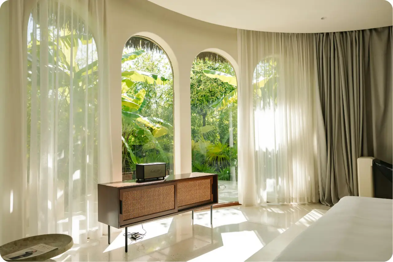 A bright, high-end private suite with floor-to-ceiling arched windows overlooking a lush garden. This confidential restorative environment for artists ensures personalized care and absolute privacy during the recovery process.
