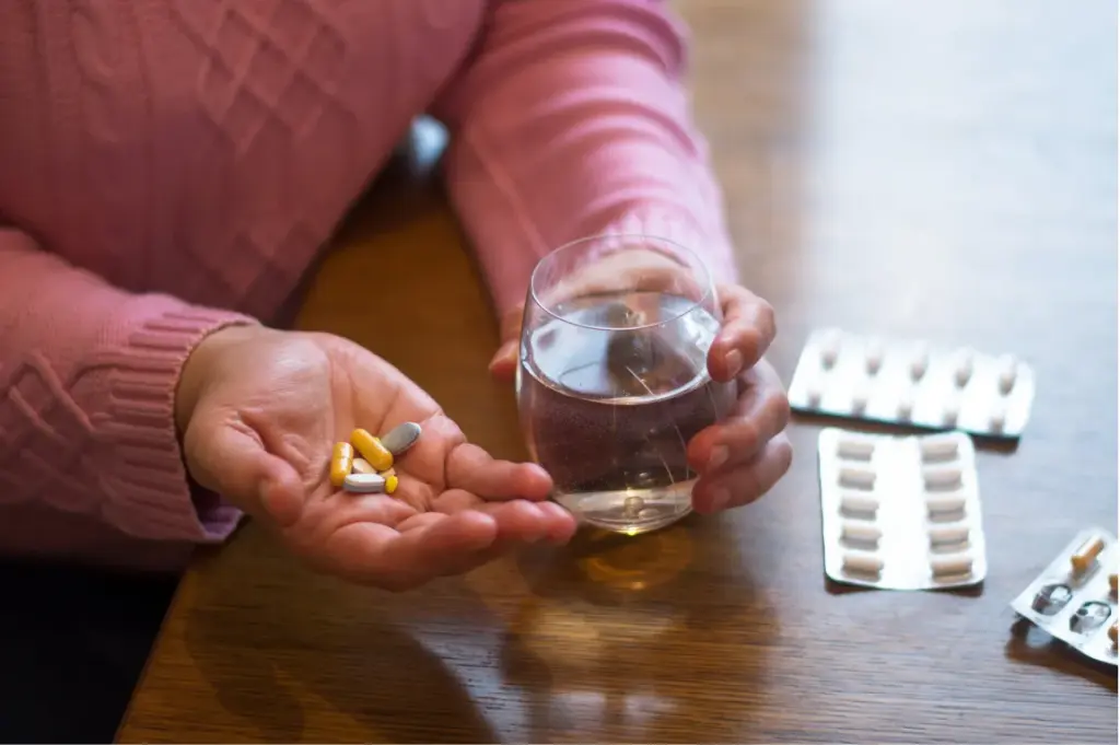 Person holding several prescription pills and a glass of water, representing tramadol use, dependence, and the risk of prescription painkiller addiction.
