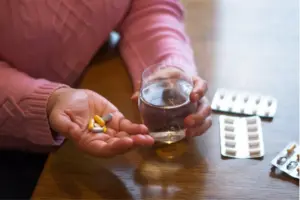 Person holding several prescription pills and a glass of water, representing tramadol use, dependence, and the risk of prescription painkiller addiction.