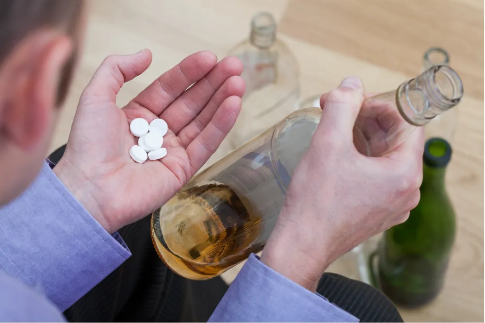 Person holding several white pills in one hand and an alcohol bottle in the other, representing the risks of combining Xanax and alcohol.